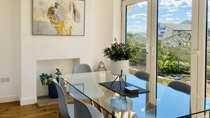 A modern dining area with a glass table, grey chairs, and a potted plant.