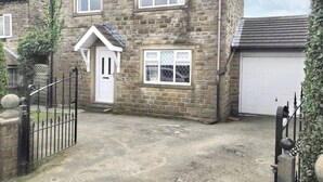 A two-story stone house with a white door and windows, a garage, and a gravel driveway.