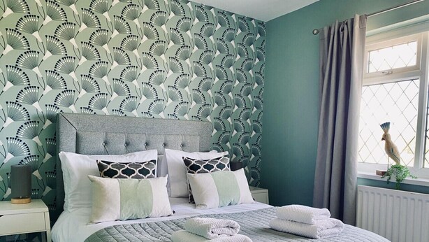 A neatly made bed with a grey quilt, white pillows, and folded towels on a nightstand.