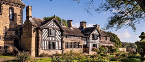 A historic building with Tudor-style architecture, featuring a large stone tower and a symmetrical facade with white timber framing.