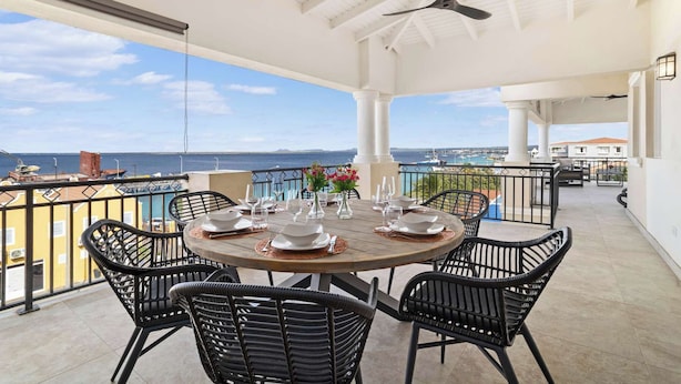 A round table set for dining with black wicker chairs, a ceiling fan, and a view of the sea and boats.