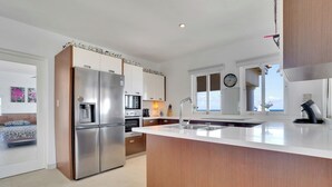 A modern kitchen with stainless steel appliances, a large island with a sink, and a view of the sea through the windows.