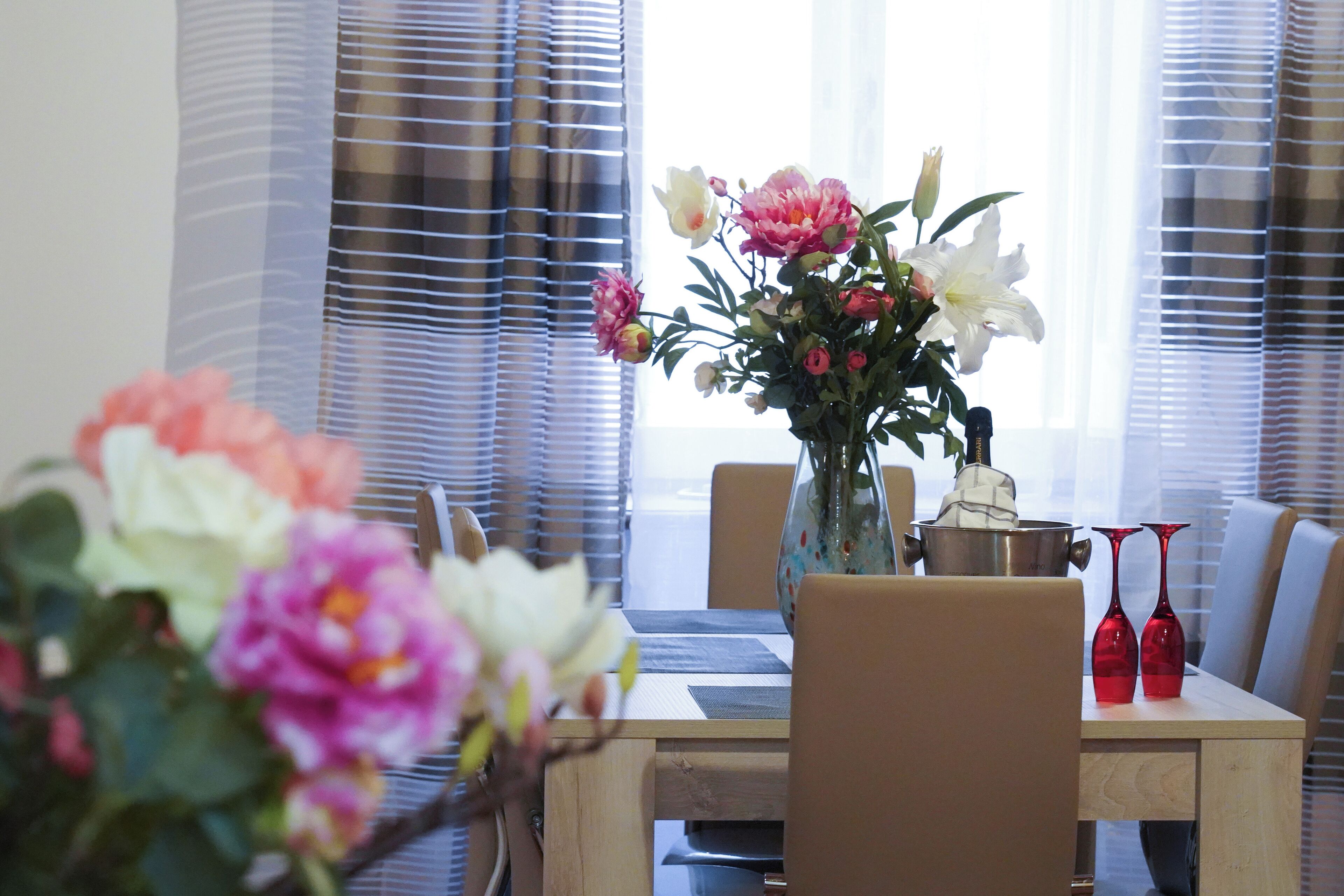 A dining table with chairs, a vase with flowers, and two red vases.