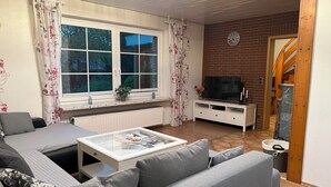 A living room with a sofa, a coffee table, a TV, and a brick wall.