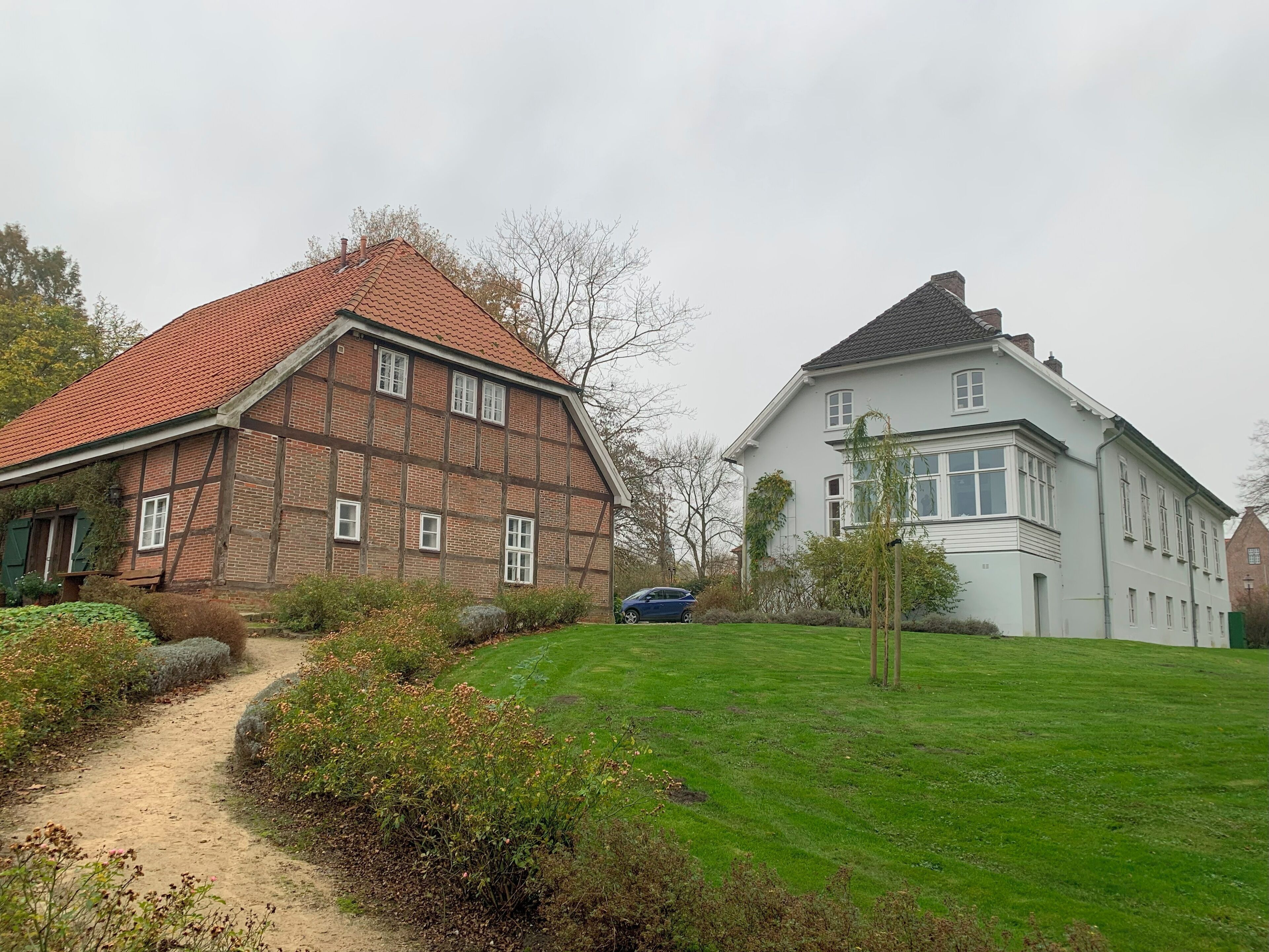 A traditional half-timbered house with a red-tiled roof and a white house with a grey roof in a suburban setting.