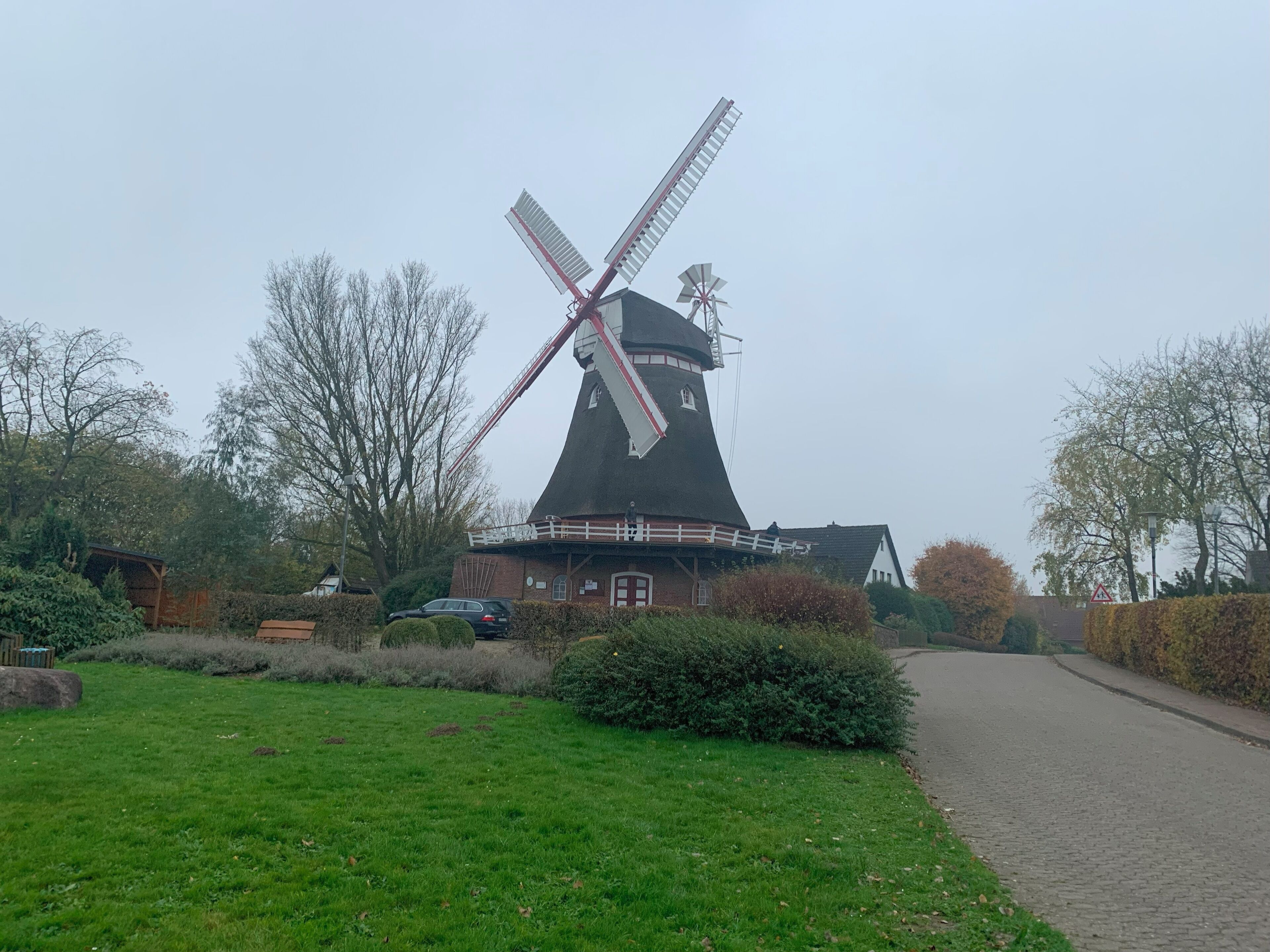 A traditional windmill with a white and red windlass, surrounded by a grassy area and a paved path.