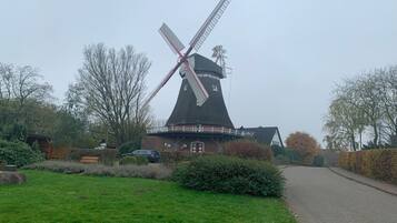 A traditional windmill with a white and red windlass, surrounded by a grassy area and a paved path.