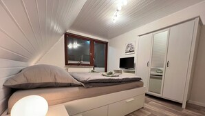 A bedroom with a bed, bedside table, TV, wardrobe, and a window with a view.