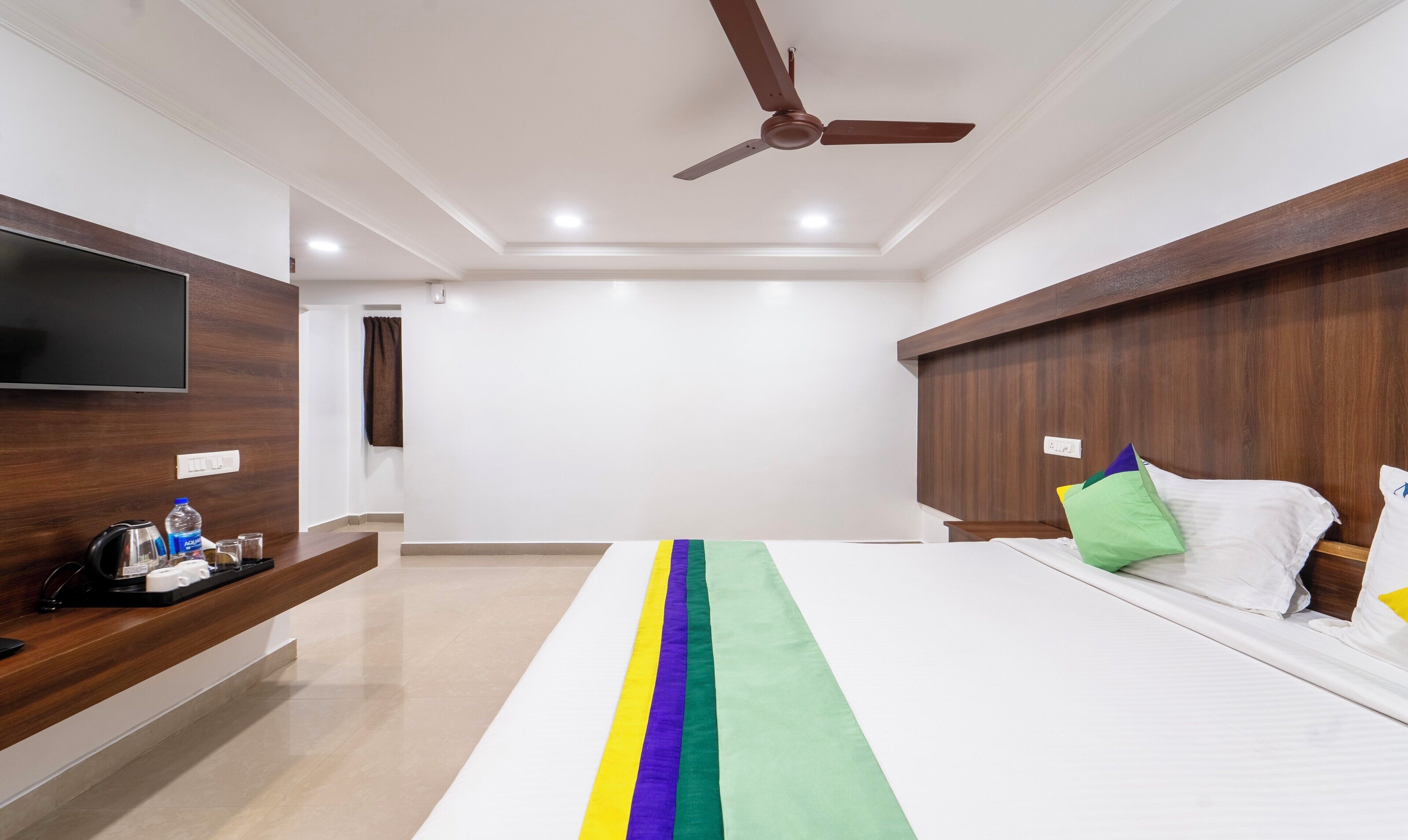A modern hotel room with a large bed, a flat-screen TV, a wooden headboard, and a ceiling fan.