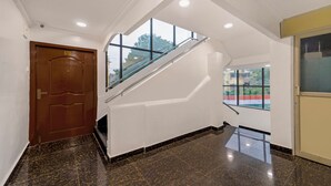 Un interior moderno con piso de mármol, puerta de madera, escalera de cristal y vistas amplias a través de grandes ventanales.