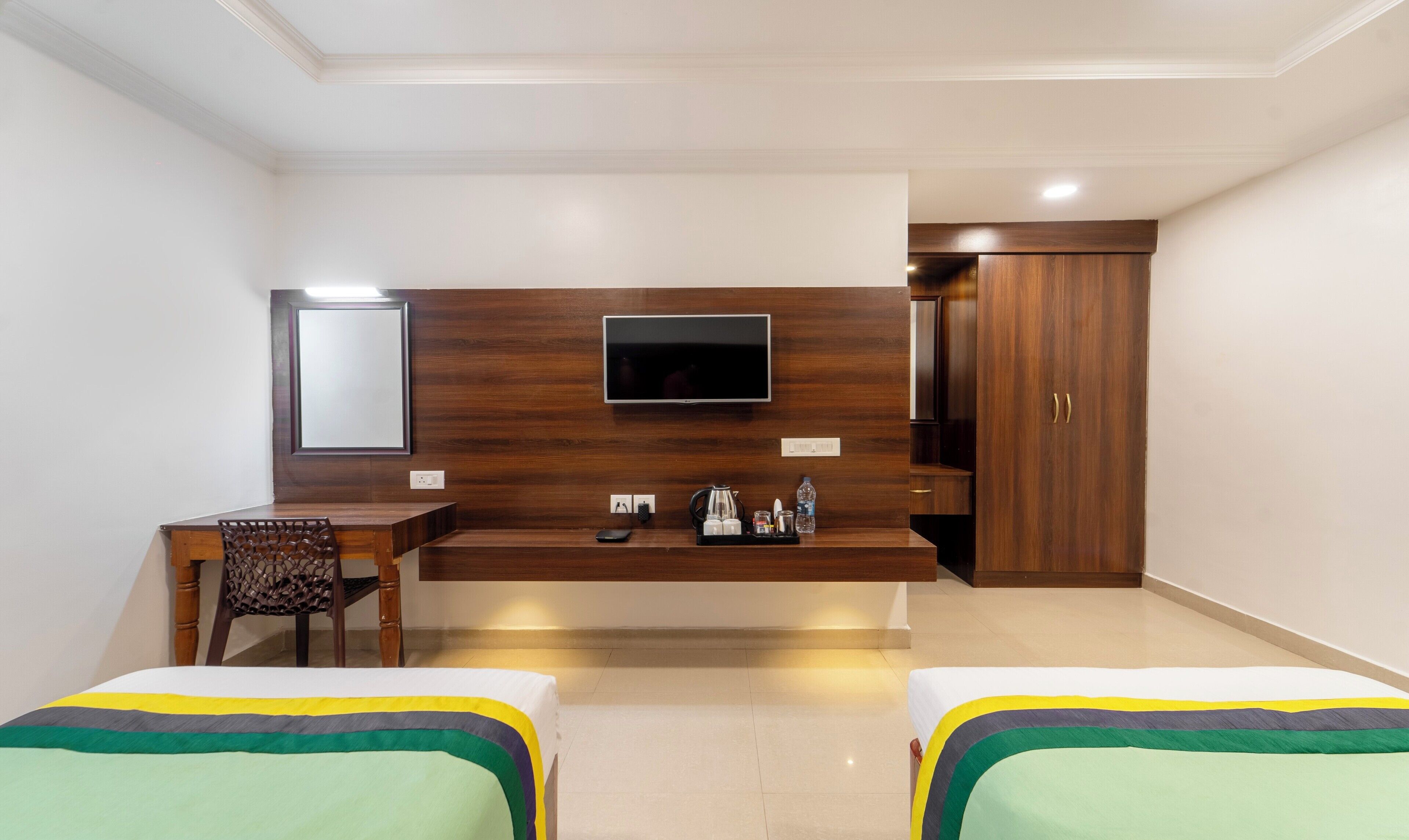 A hotel room with a wooden desk, a flat-screen TV, a wardrobe, and two beds with colorful bedding.