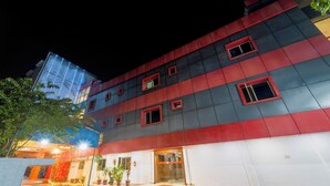 A modern building with a red and grey facade, multiple windows, and a visible entrance. - NVR RESIDENCY (Chennai)