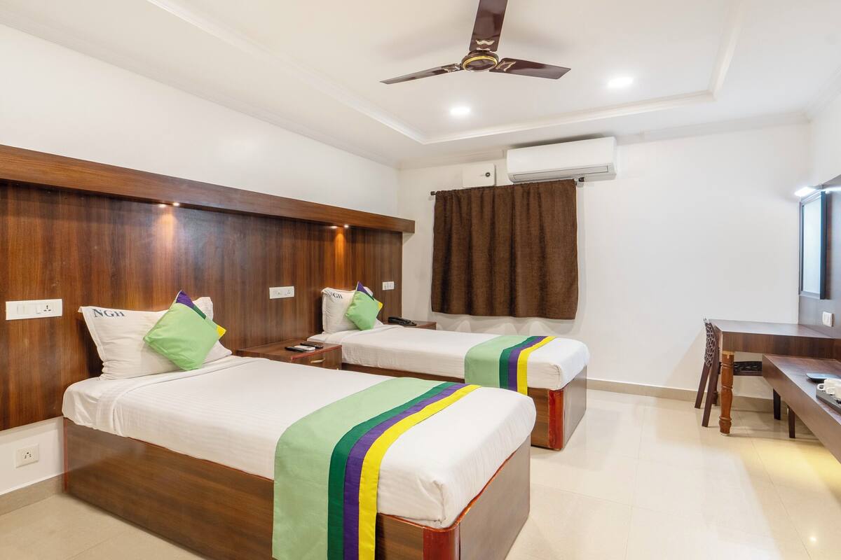 A hotel room with two single beds, wooden headboards, a desk, and a ceiling fan.