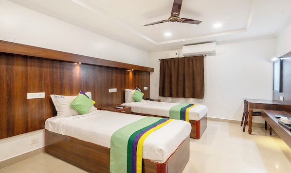 A hotel room with two single beds, wooden headboards, a desk, and a ceiling fan. - NVR RESIDENCY (Chennai)