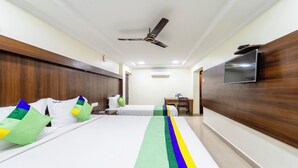 A hotel room with two beds, a ceiling fan, a TV mounted on the wall, and a small table with a chair. - NVR RESIDENCY (Chennai)