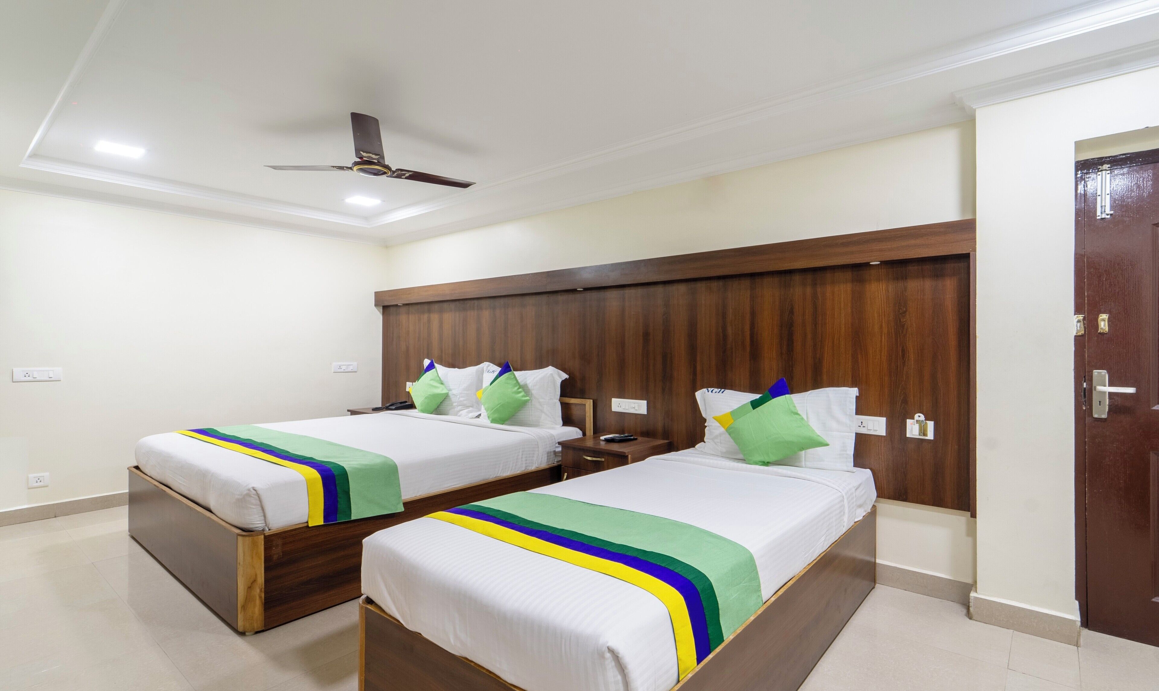 A hotel room with two single beds, a wooden headboard, a ceiling fan, and a door with a key lock.