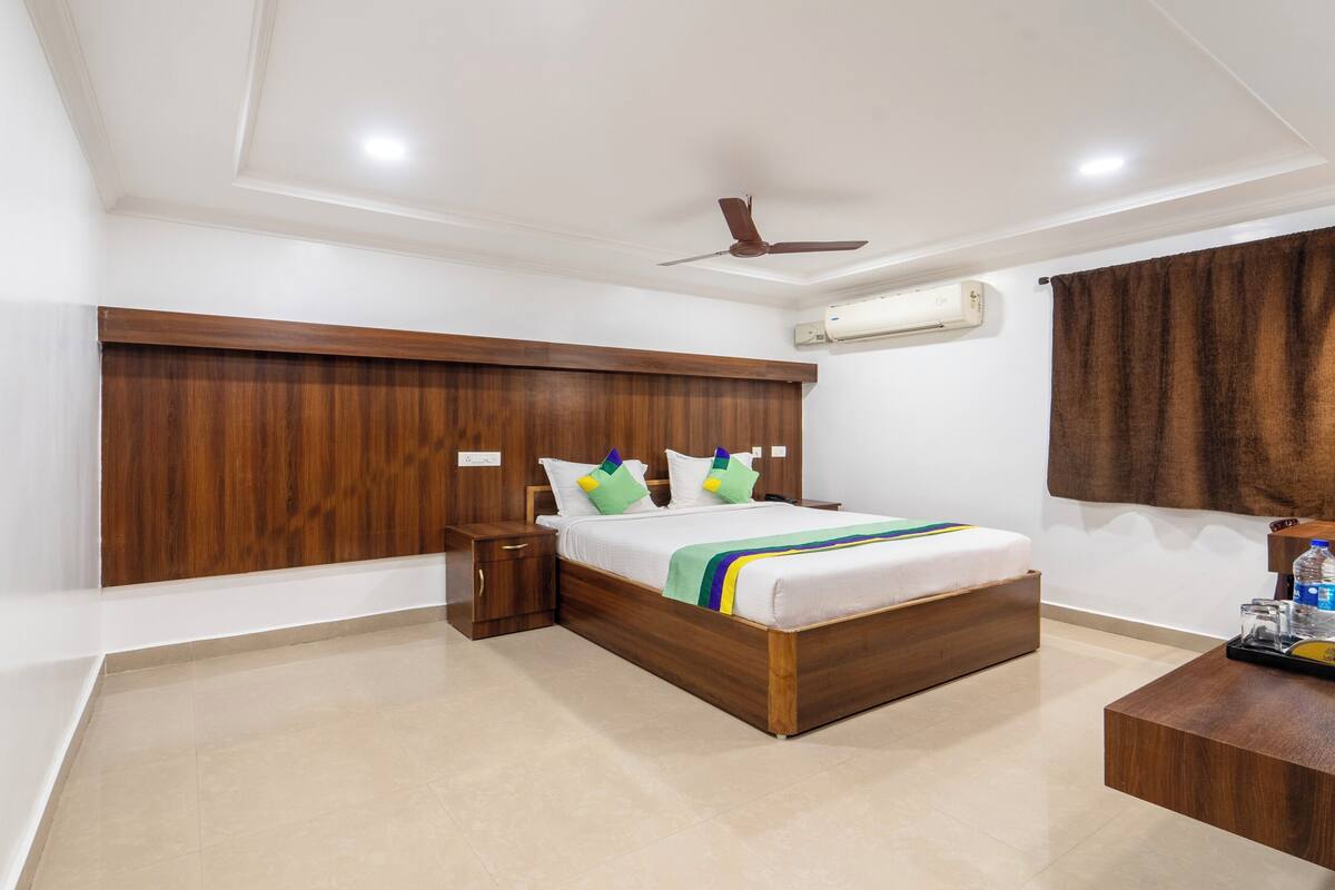 A modern hotel room with a wooden headboard, a bed with a colorful striped blanket, a nightstand, a wooden side table, and a ceiling fan.