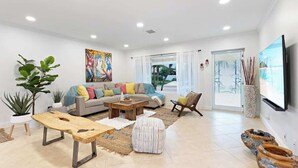 A modern living room with a sofa, coffee table, and ottoman, a large painting, and a TV on the wall. - Beach Walk Villa with Waterfall Pool LBTS (Lauderdale-by-the-Sea)