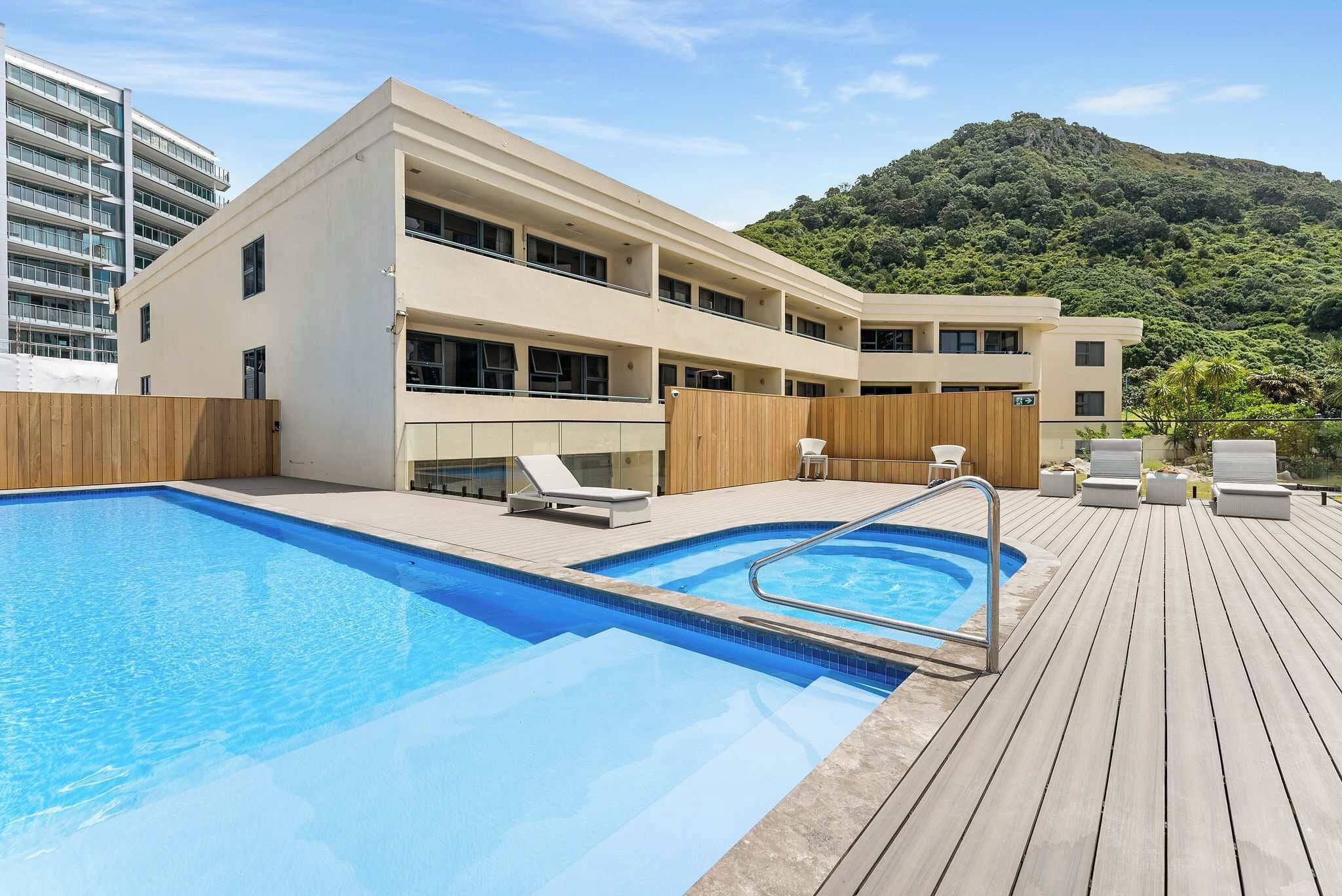Un hôtel moderne doté d’une piscine, d’une terrasse en bois et offrant une vue sur une colline verdoyante.