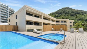 Un hotel moderno con piscina, terraza de madera y vista a una colina verde exuberante.