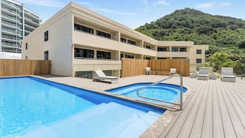 Un hôtel moderne doté d’une piscine, d’une terrasse en bois et offrant une vue sur une colline verdoyante.