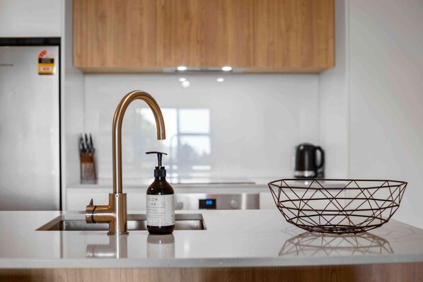 A modern kitchen with a stainless steel sink, a gold faucet, and a black bottle of hand soap. - Oceanside Retreat Mount Maunganui (Mount Maunganui)
