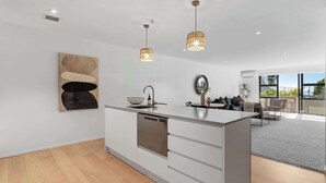 Cocina moderna con armarios blancos, una isla central, iluminación colgante y un amplio ventanal con vistas a zonas verdes.