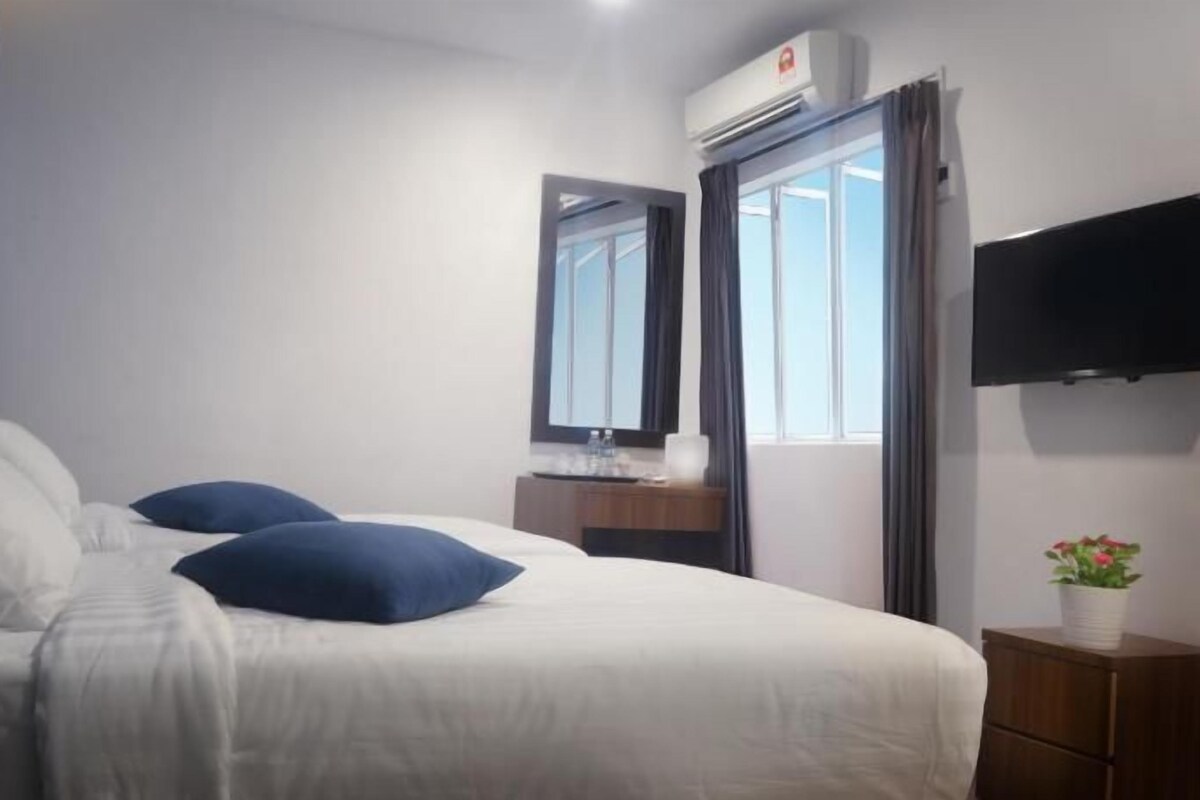 A hotel room with a bed, a bedside table, a mirror, a TV, and an air conditioning unit.