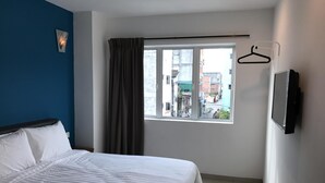 Une chambre d’hôtel avec un lit, une fenêtre avec des rideaux, un téléviseur fixé au mur et une vue sur les bâtiments environnants.