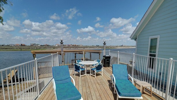 A deck with two sun loungers and a table, overlooking a body of water. - Canal Views & Pool | 2 Min to Beach | Fishing Pier (Corpus Christi)