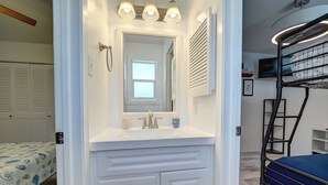 A bathroom with a white vanity, a mirror, a sink, and a shower area. - Canal Views & Pool | 2 Min to Beach | Fishing Pier (Corpus Christi)