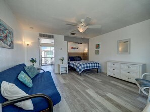 A bedroom with a bed, a dresser, a chair, a ceiling fan, and a view of the outside.