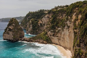 A coastal landscape with cliffs, a beach, and a clear view of the ocean.