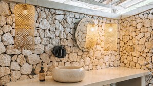 A stone wall bathroom with a large basin, hanging lights, and a bottle of hand soap. - The Raja Lima (Penida Island)