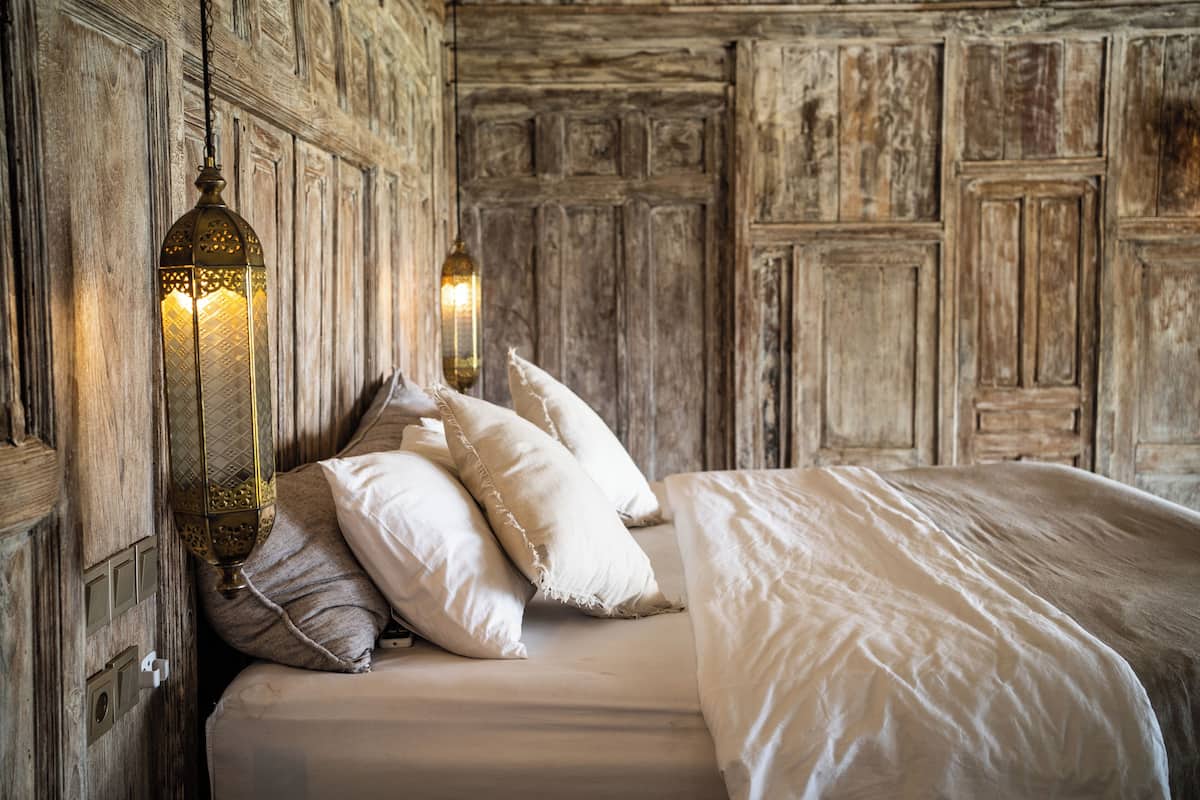 Un letto con lenzuola bianche, due applique decorative e un pannello di legno a parete.