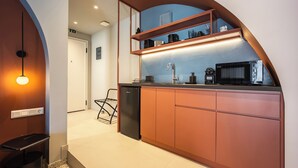 Cocina moderna con horno empotrado, microondas y cafetera. Se observa un lavamanos pequeño y un refrigerador negro. La cocina presenta un diseño con arco curvo y una encimera con estante integrado.