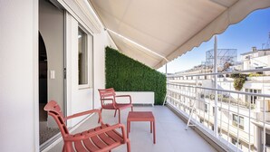 Un balcón con tres sillas rojas, una mesita pequeña, un toldo blanco y una pared verde.