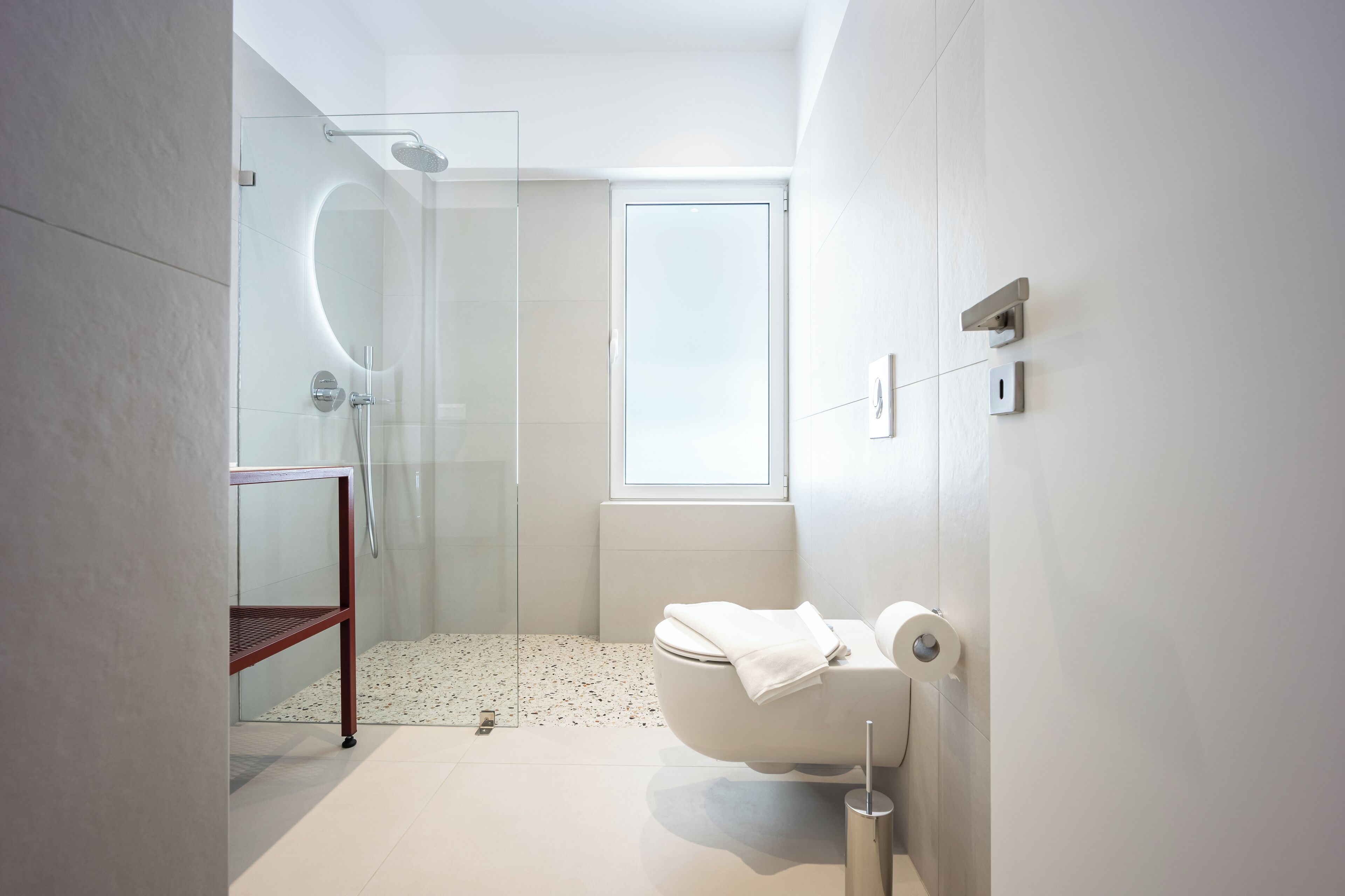 A modern bathroom with a glass shower enclosure, a toilet, and a small shelf.