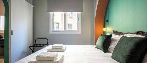 A hotel room with a bed, a window, a chair, and an air conditioning unit.