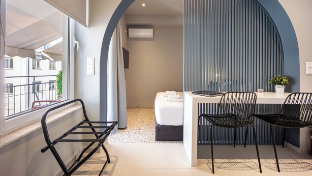 Una habitación de hotel moderna con un ventanal grande, una cama, un escritorio con dos sillas y un panel decorativo en la pared.