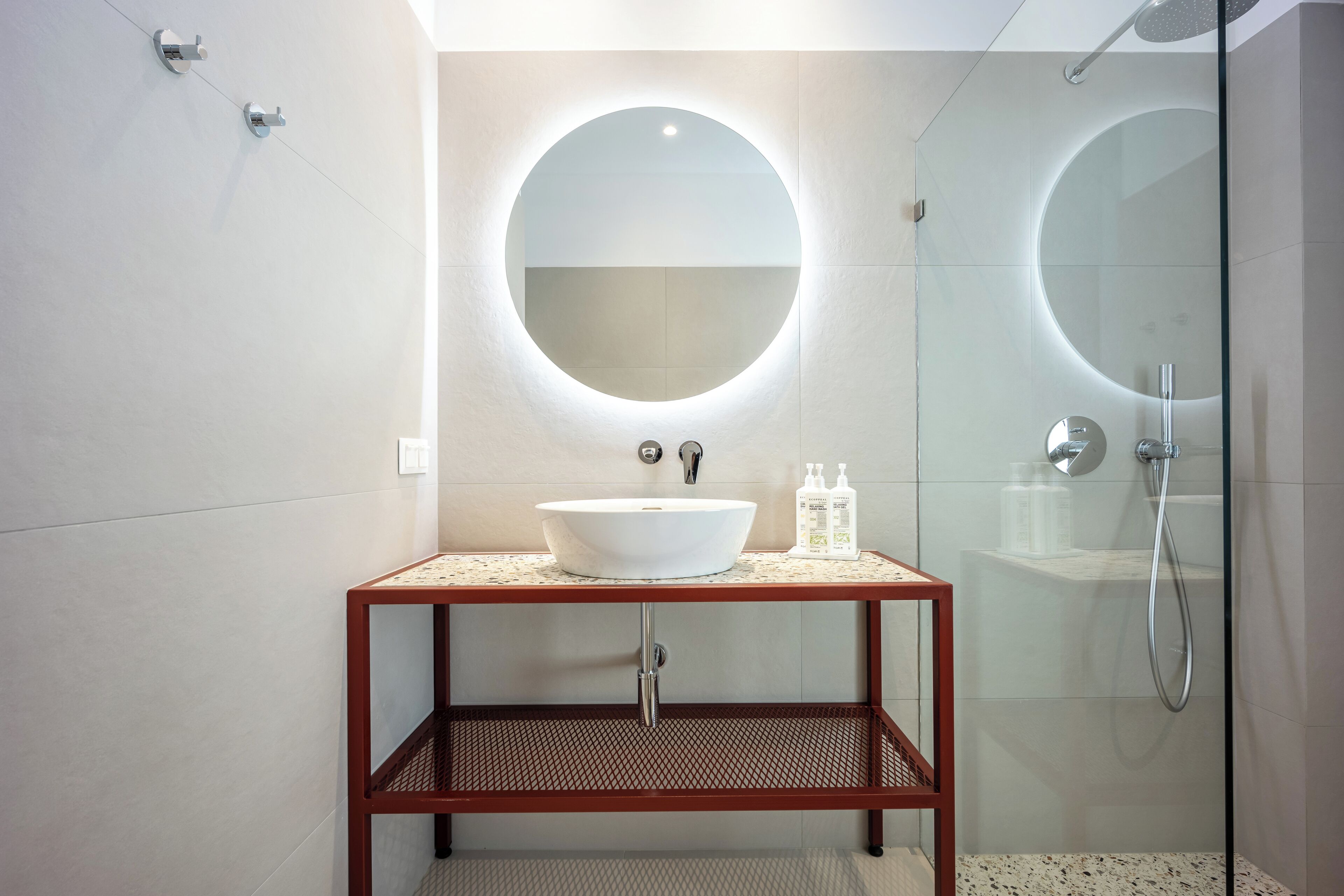 A modern bathroom with a round mirror, a white sink, and a glass-enclosed shower.