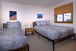A bedroom with two beds, a nightstand, and a window with blinds.
