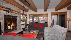 Een gezellige woonkamer met een open haard, een zithoek en uitzicht op een besneeuwd berglandschap.