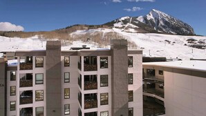 Un hôtel à plusieurs étages, doté de balcons et de grandes fenêtres, qui se dresse sur fond de montagnes enneigées.