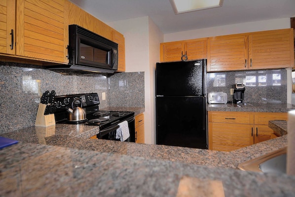 A kitchen with granite countertops, a black stove, a black refrigerator, wooden cabinets, and a microwave.