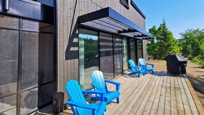 Un edificio moderno con terraza de madera, ventanas grandes y sillas azules.
