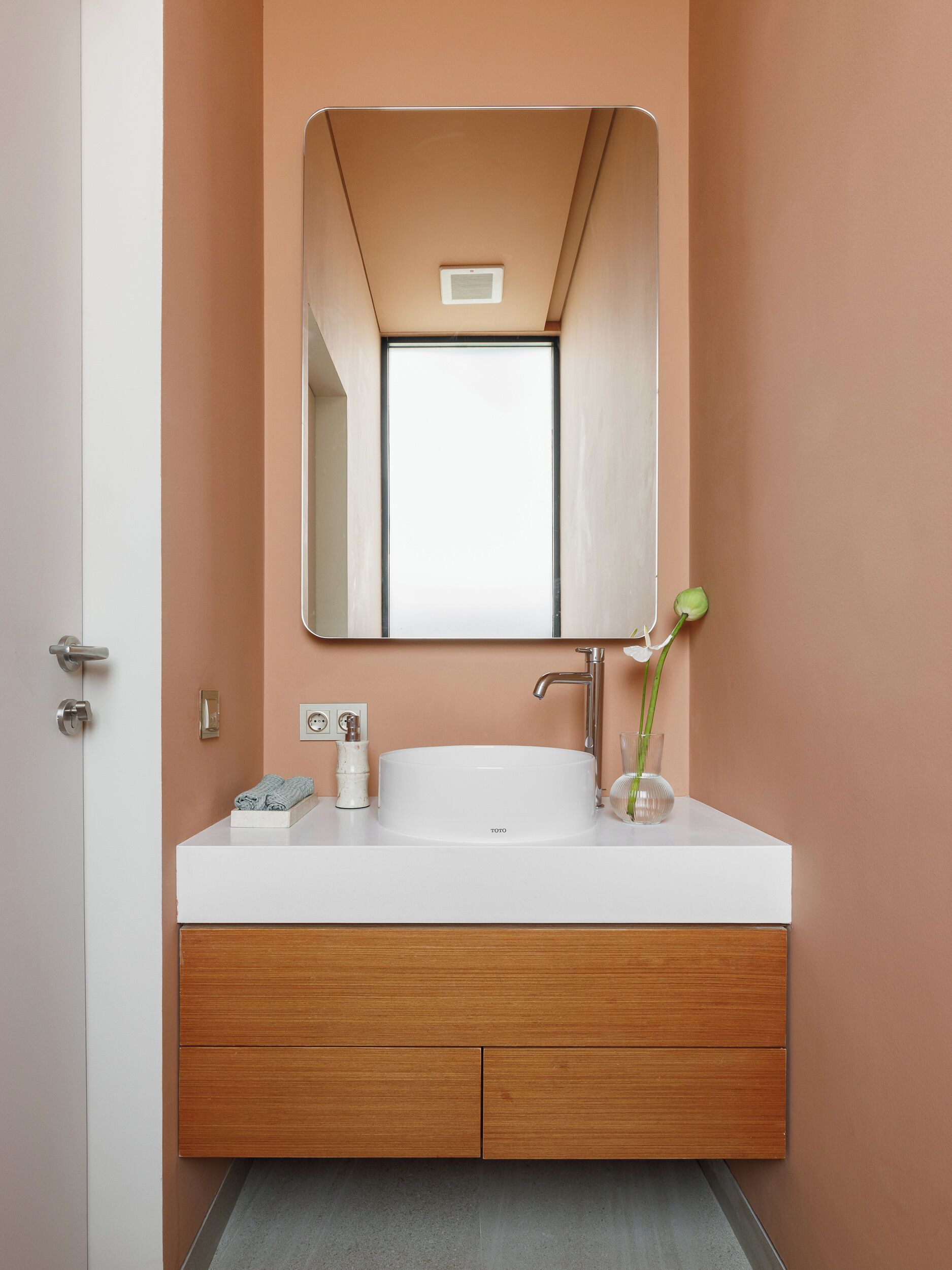 Un baño con lavamanos blanco, tocador de madera y un espejo sobre el lavamanos.