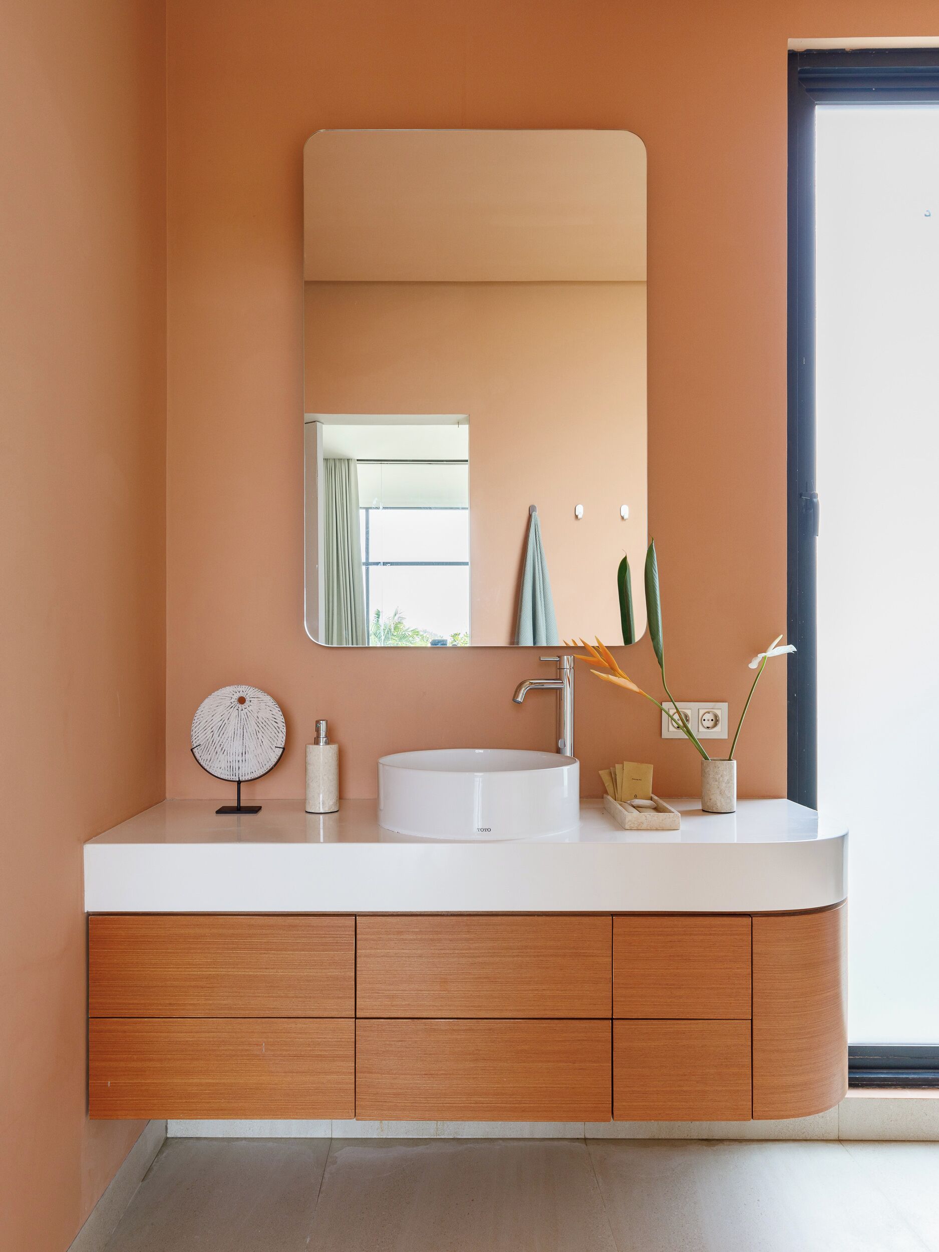 Een moderne badkamer met een witte wastafel, houten kastjes en een grote spiegel.