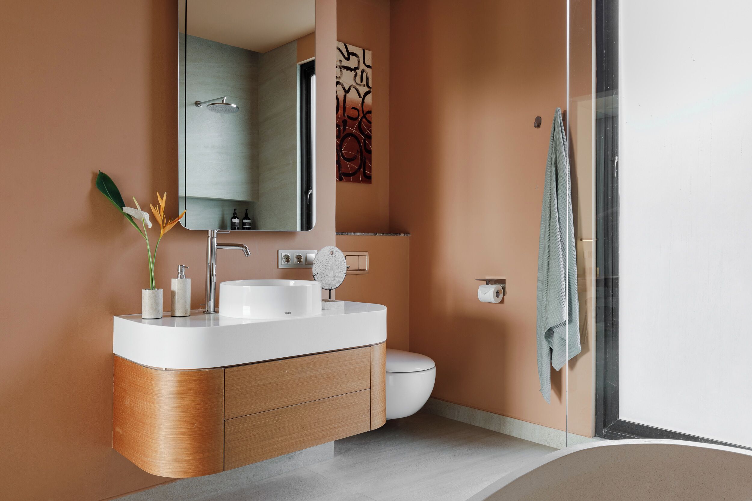 A modern bathroom with a curved vanity, a toilet, and a glass shower enclosure.