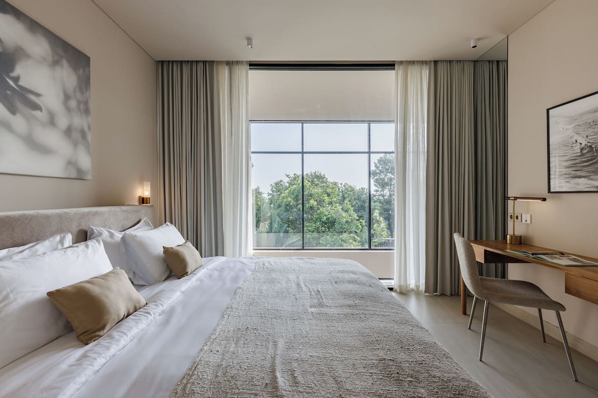 Ein modernes Schlafzimmer mit einem großen Bett, einem Schreibtisch und Blick auf Bäume durch das Fenster.